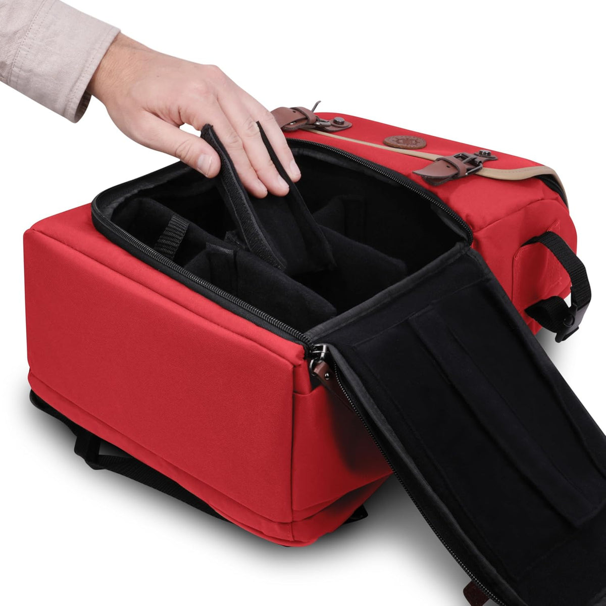A hand adjusts a padded divider inside an open red camera bag with brown leather accents.