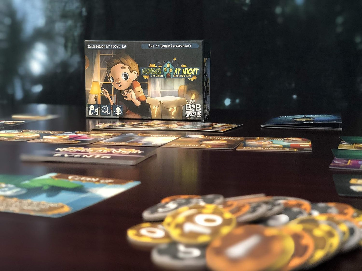 The "Noises at Night" deduction game box, featuring a scared boy, is displayed with cards and tokens on a table.