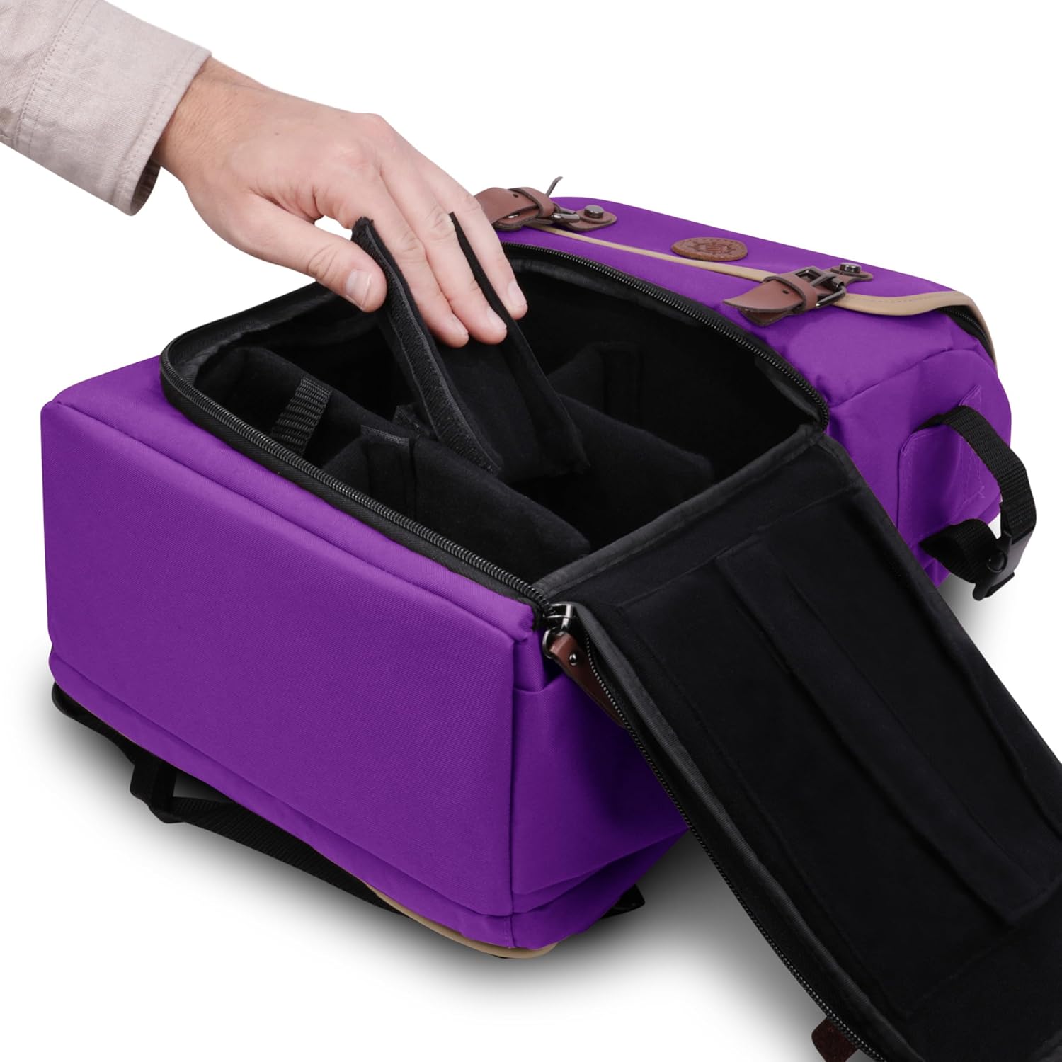 A hand places a black padded divider inside an open purple camera bag with brown leather accents.