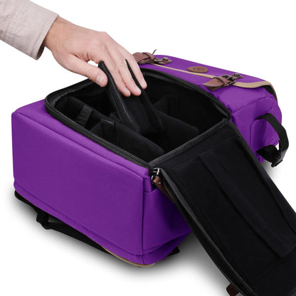A hand places a black padded divider inside an open purple camera bag with brown leather accents.