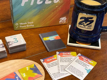 Overhead shot of the board game Canvas with paint tiles score track cards and a coffee mug