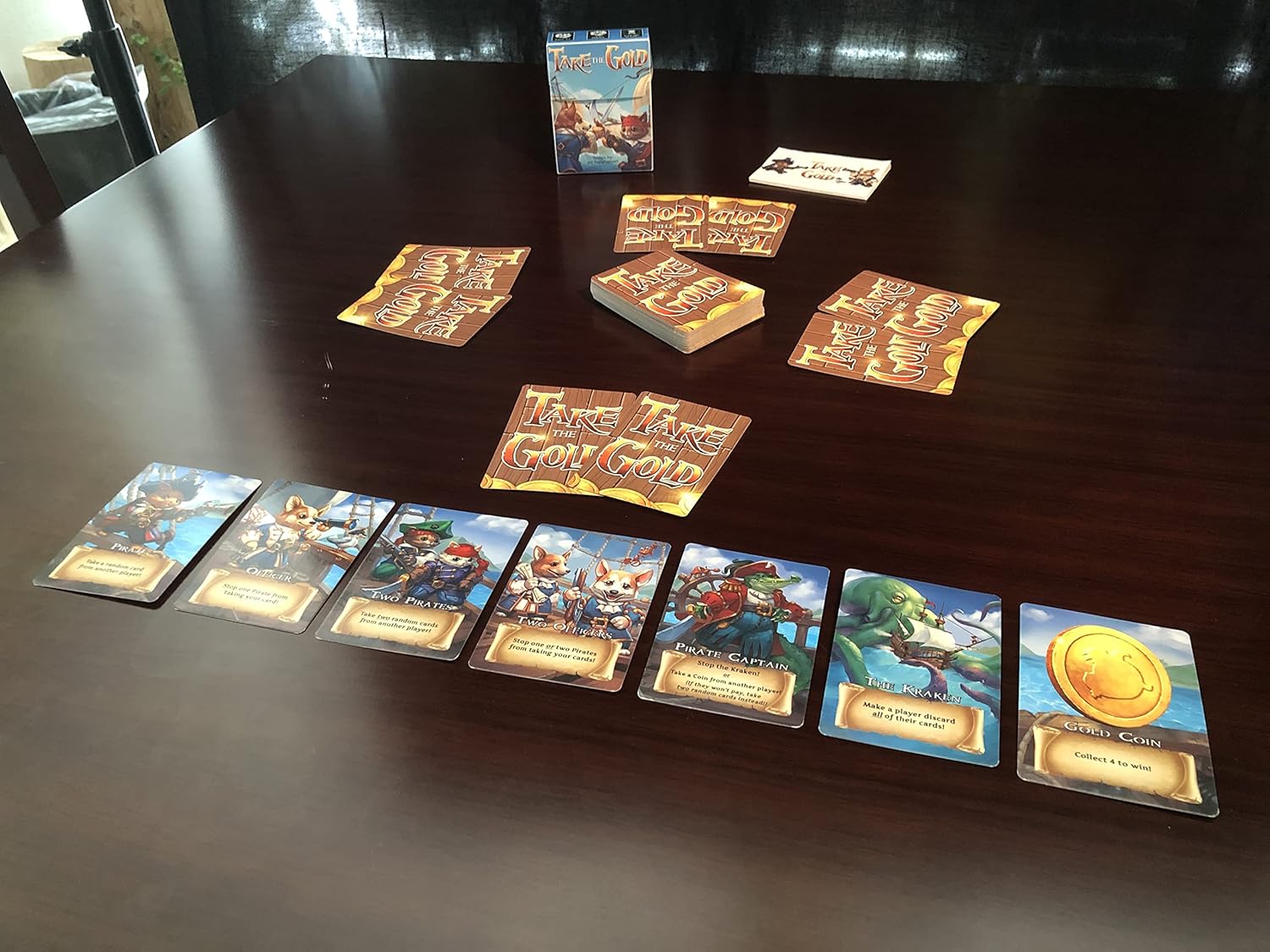 A pirate-themed "Take the Gold" card game laid out on a dark table, showing character and gold coin cards.