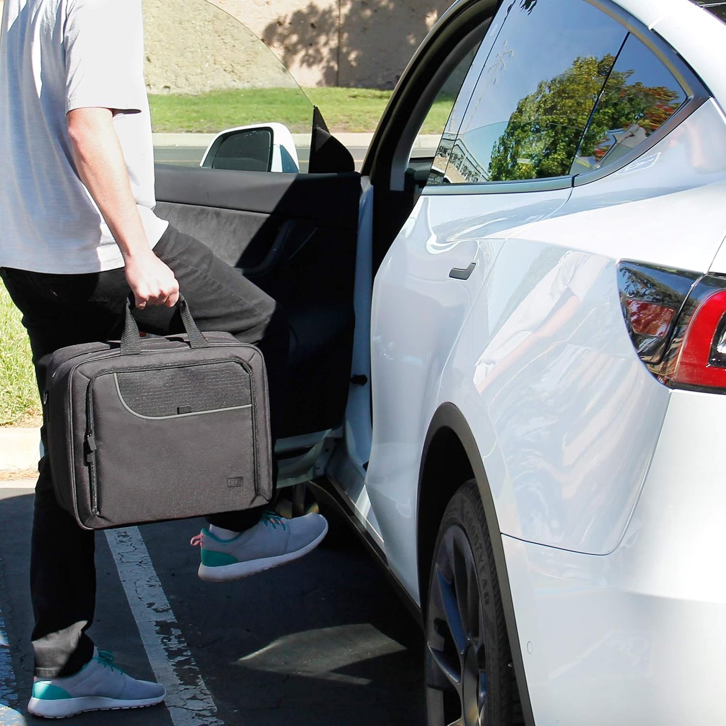 A person with a black briefcase steps into a white Tesla.
