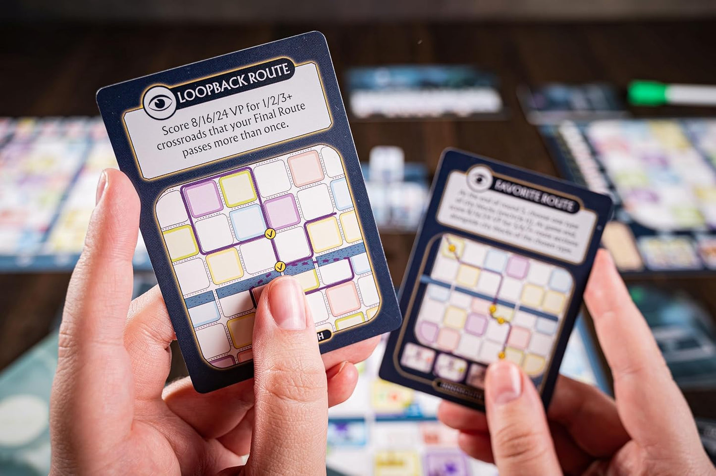 Close-up of hands holding two route-building board game cards, one titled "Loopback Route."