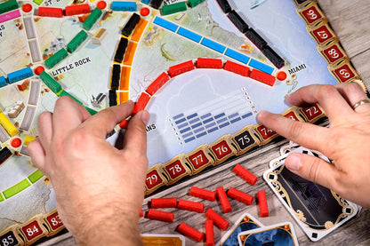 Hands placing red train cars on a colorful board game map while scoring points on the track