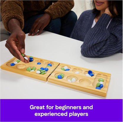 Two people playing Mancala, A hand places blue, green, and white pieces on the wooden game board