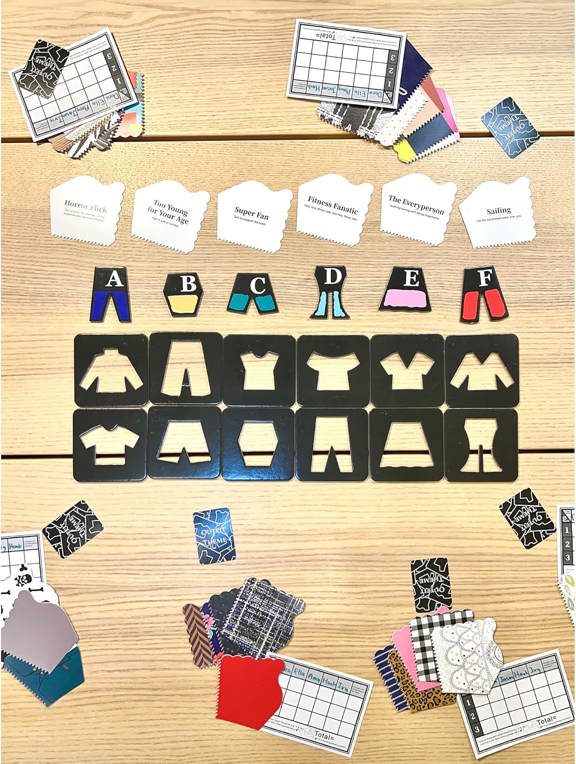 An outfit design board game laid out on a table. It shows theme cards, colorful clothing pieces, and black garment tiles