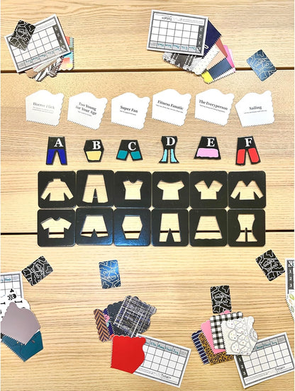 An outfit design board game laid out on a table. It shows theme cards, colorful clothing pieces, and black garment tiles