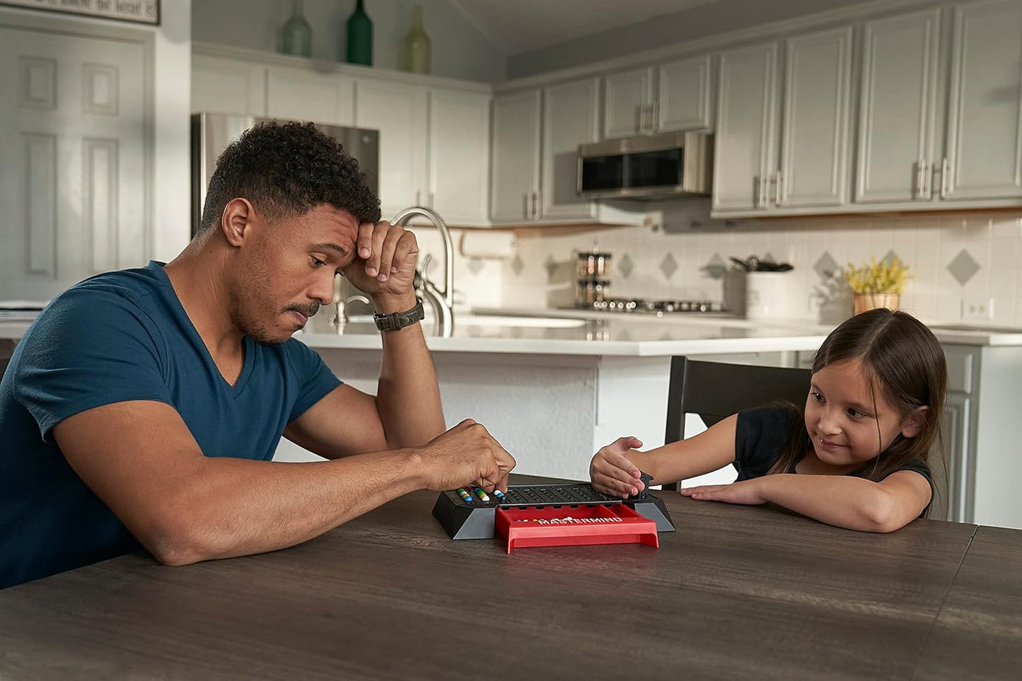 Father and daughter playing the Mastermind board game intently at a kitchen table