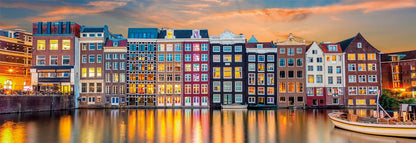 Colorful row of gabled houses reflecting glowing lights onto a dark canal at sunset