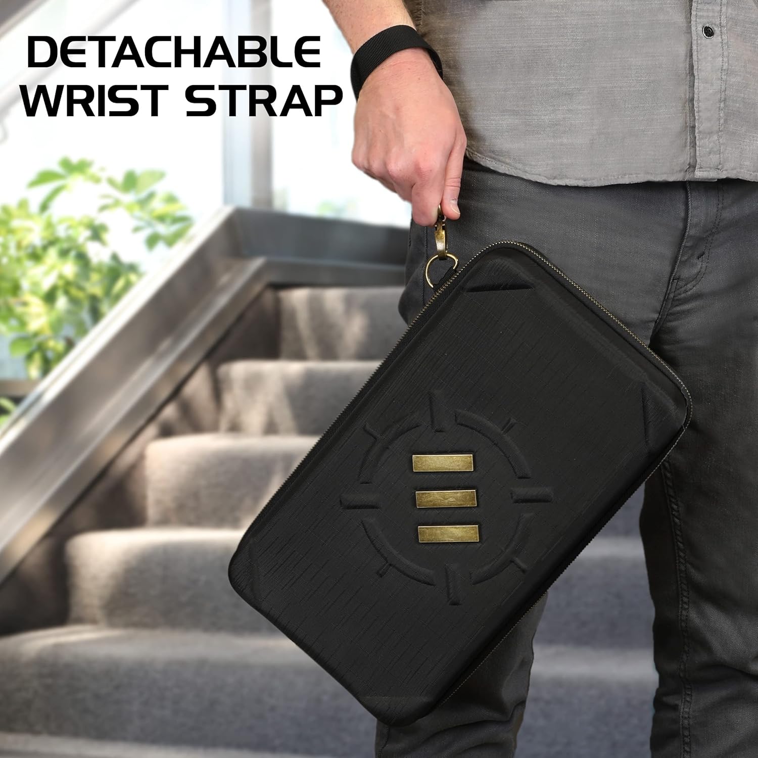 A person holds a black textured zippered case with a gold logo and a detachable wrist strap