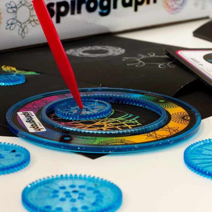 Spirograph scratch art kit with rainbow designs on black paper and a red pen drawing in a blue plastic gear