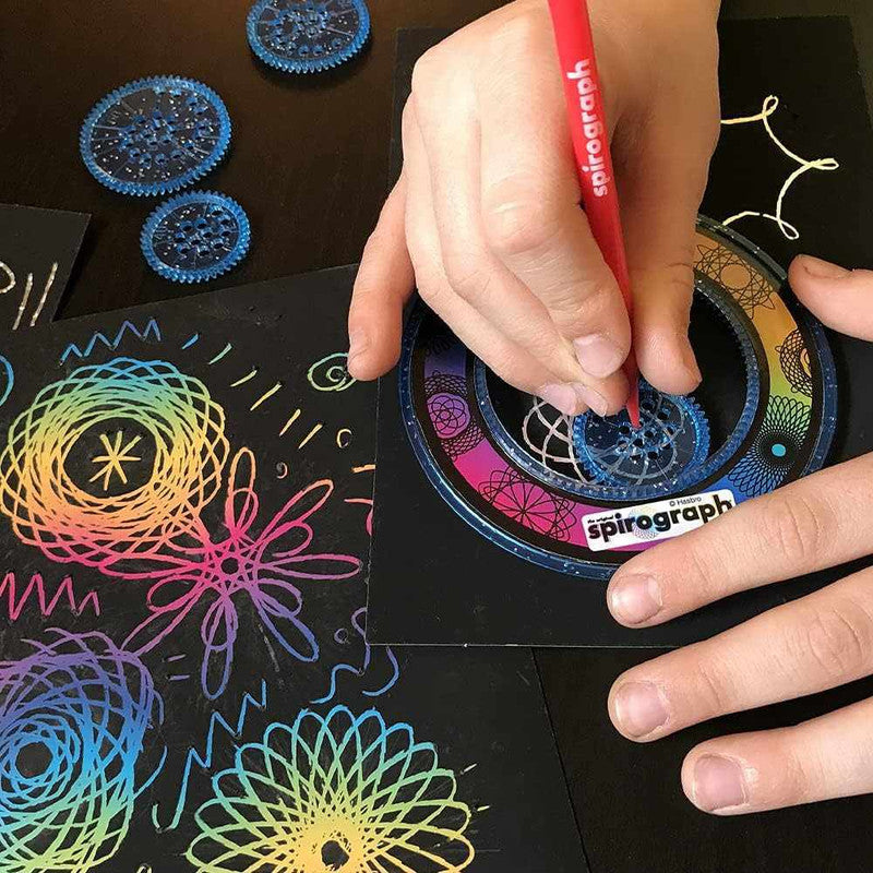 Child uses red Spirograph pen and wheel to create colorful designs on black paper
