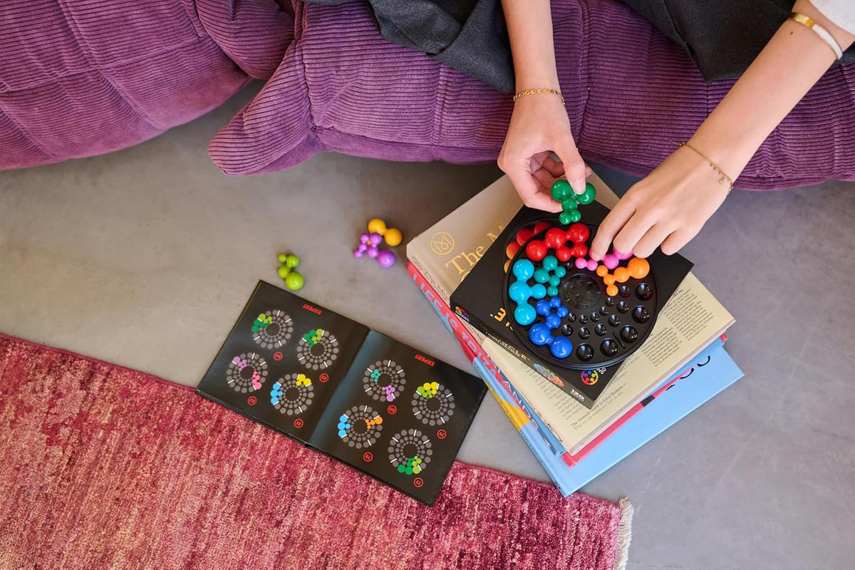 Overhead view of hands placing a green puzzle piece onto a colorful, circular brain game board resting on books