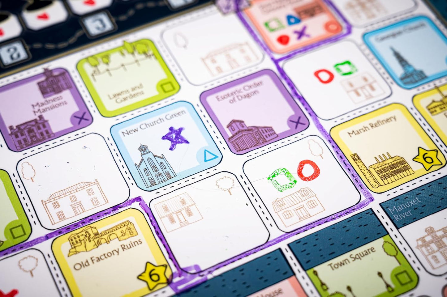 Colorful board game map showing labeled location tiles, hand-drawn buildings, and placement symbols
