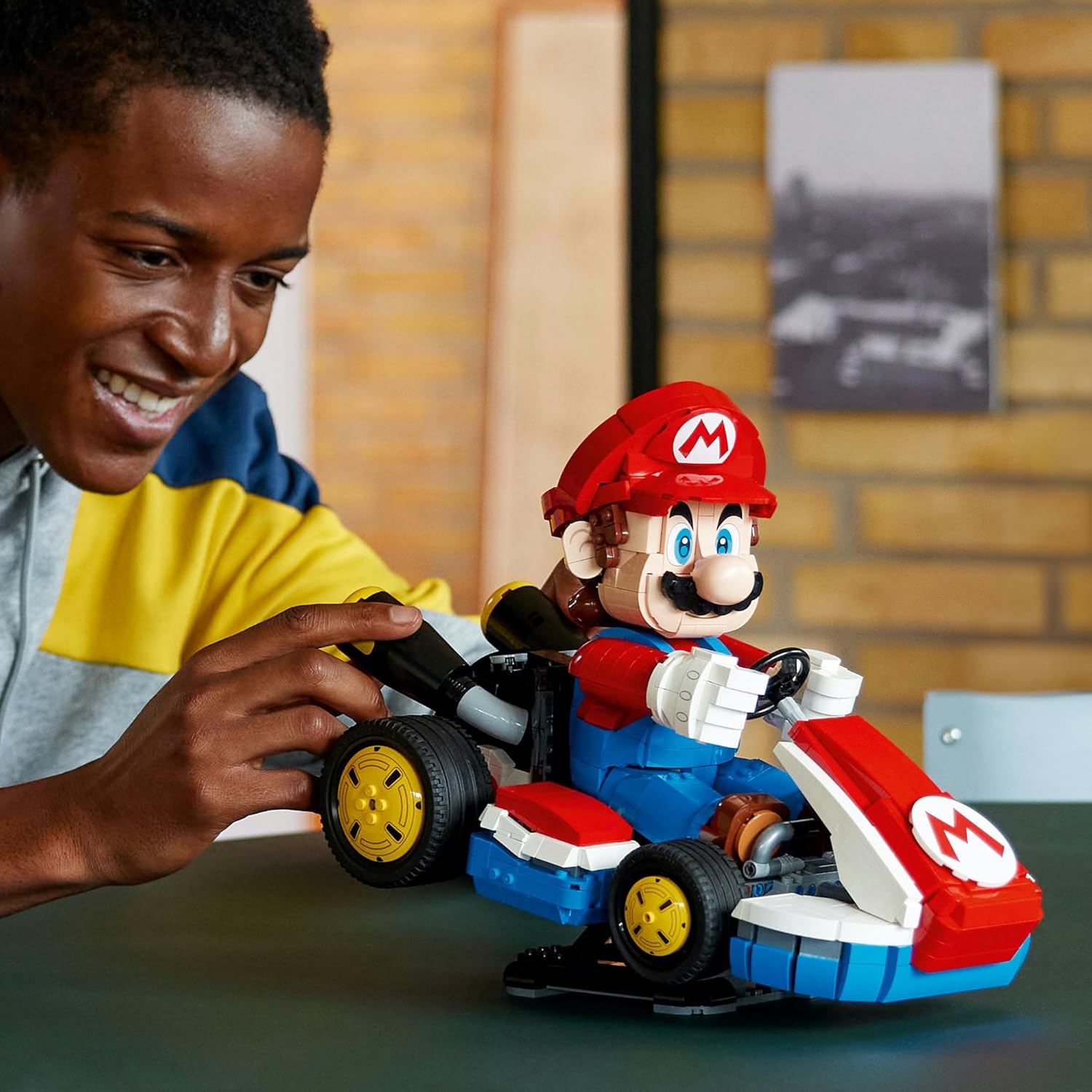 Smiling man interacts with a large LEGO Mario figure driving a Kart model