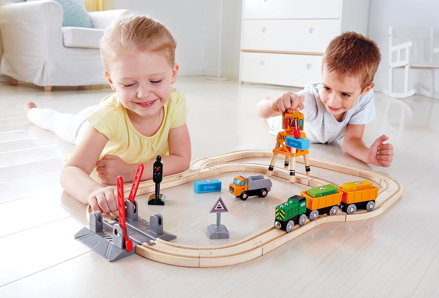 Two happy children lying on the floor playing with a wooden train set and colorful crane toy