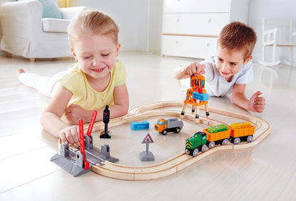Two happy children lying on the floor playing with a wooden train set and colorful crane toy