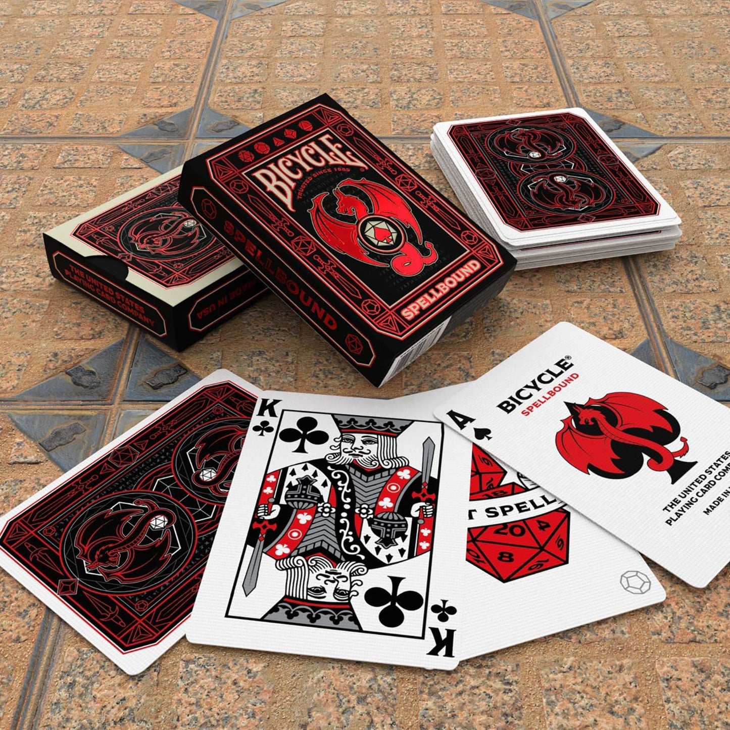 Black and red Bicycle Spellbound playing cards scattered on a tile floor, featuring dragon designs and a King card