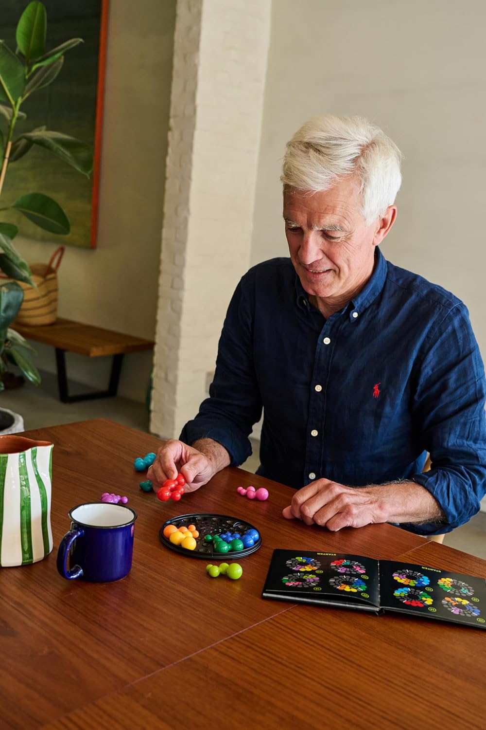 Senior man focused on assembling a IQ Deluxe Circle puzzle with connected plastic pieces on a wooden table
