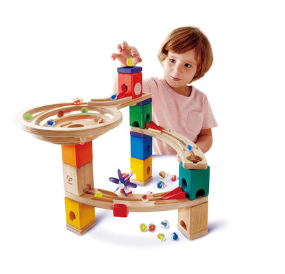 Child drops marble into a wooden marble run toy built with colorful blocks