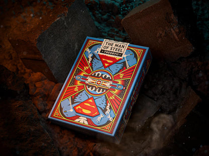 Superman "The Man of Steel" playing card tuck box with stylized comic art, displayed on dark rocks