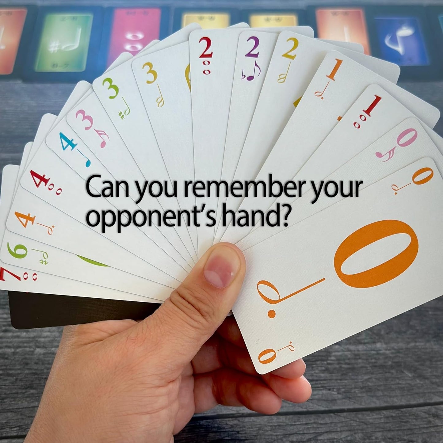 A hand holds a fan of white game cards with colorful numbers and music symbols over a dark table.