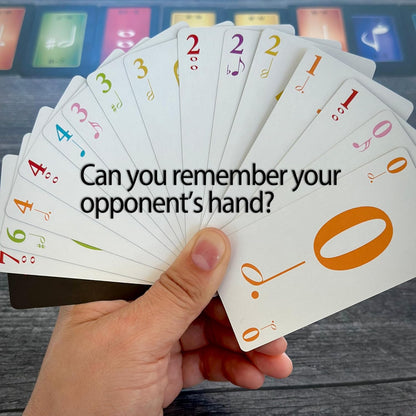 A hand holds a fan of white game cards with colorful numbers and music symbols over a dark table.