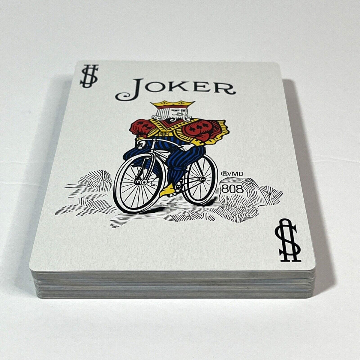 A Bicycle 808 Joker playing card showing a crowned figure riding a bicycle, atop a stack of cards