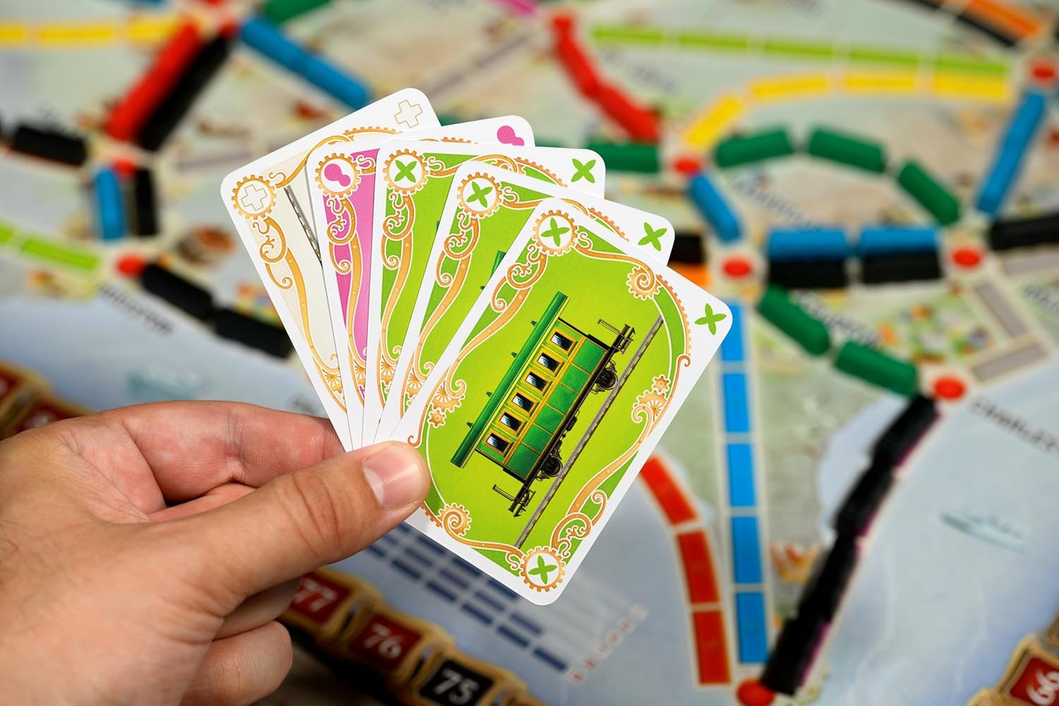 Hand holding green train cards over a board game map (Ticket to Ride) with colored route tokens