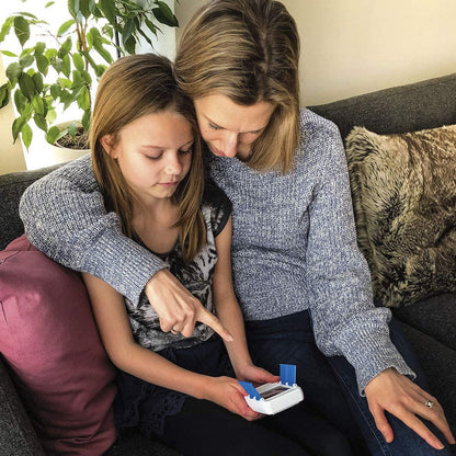 Mother and daughter pointing at a white and blue product likely related to DNA testing or similar biological sample analysis