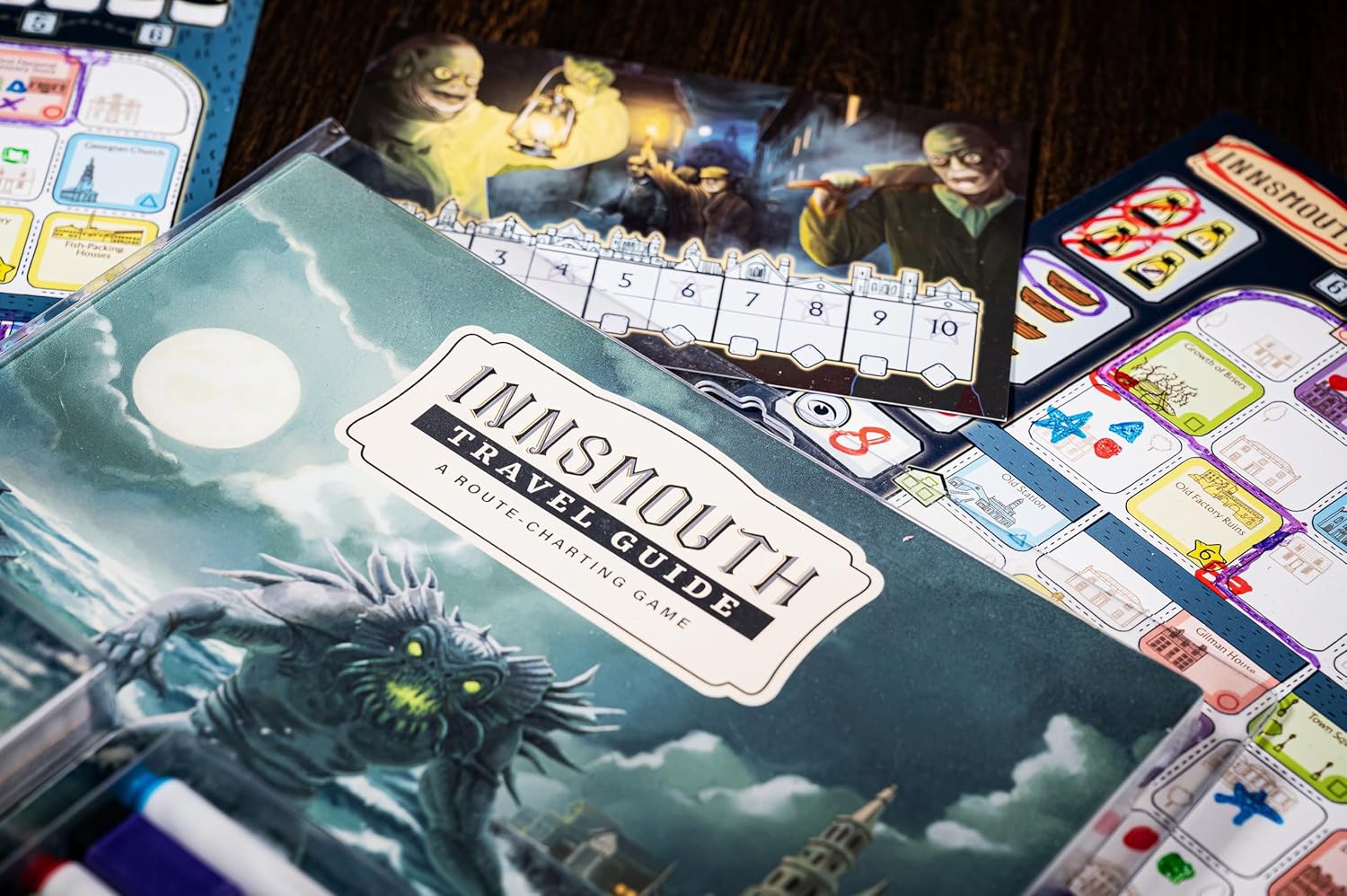 Cover of the "Innsmouth Travel Guide" board game, showing a monster under a full moon, with surrounding map boards and cards