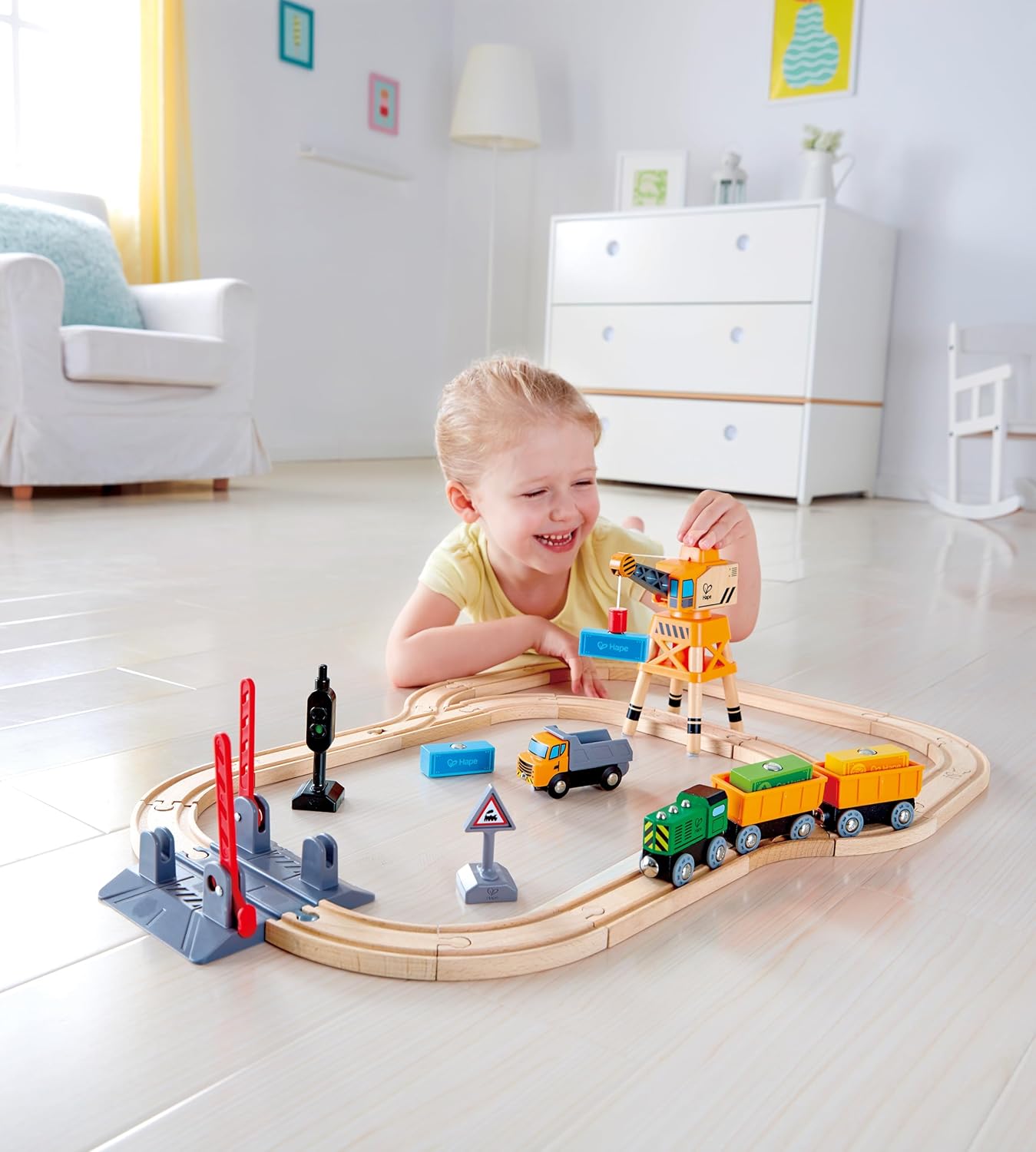 Smiling child playing with a wooden train set, using a toy crane to load cargo