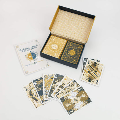 An open box of 'Illuminated Playing Cards' with two decks -  a rulebook -  and gold and blue designed cards fanned out