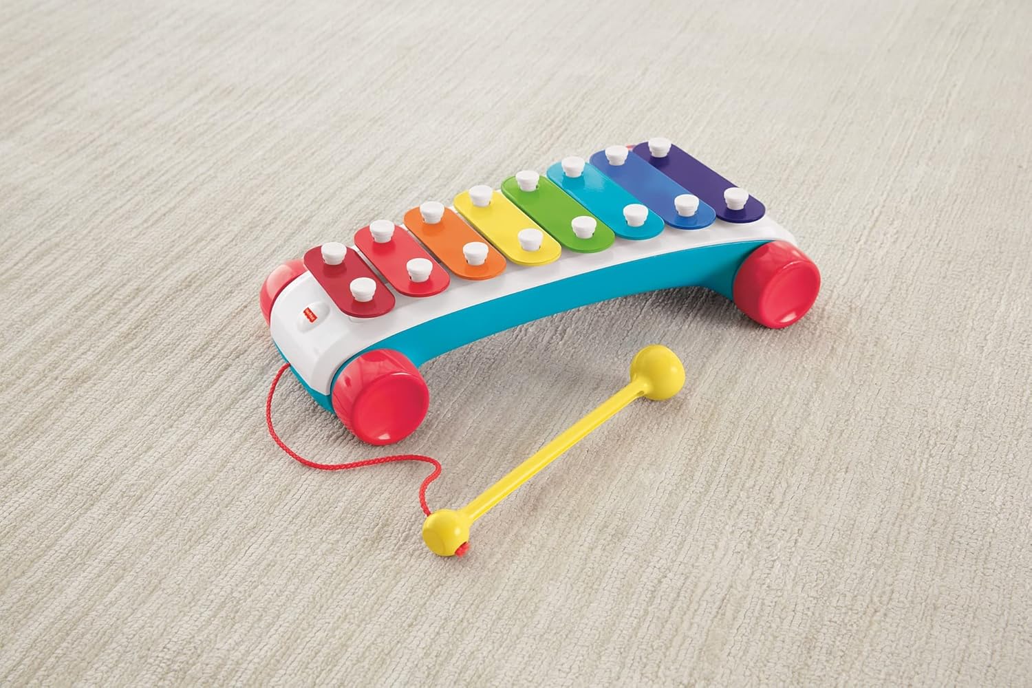 A children's pull-along xylophone with rainbow keys -  red wheels -  and a yellow mallet on light carpet