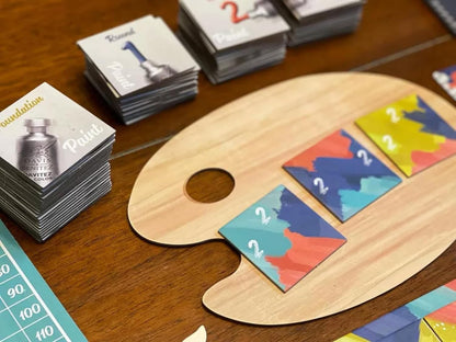 Paint Splatter Game Cards stacked on a wooden artist's palette and table