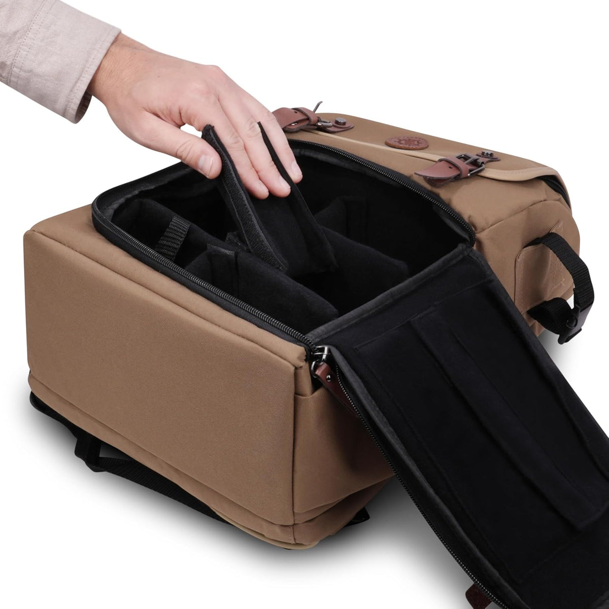 A hand adjusts a black padded divider inside an open tan camera bag with leather accents.