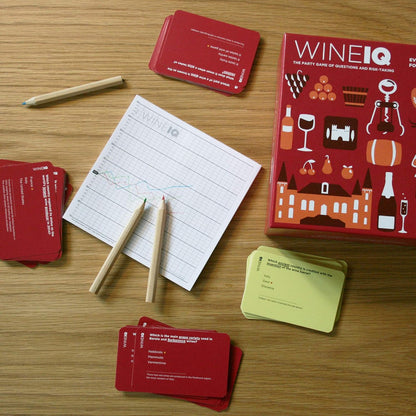 Overhead shot of the Wine IQ party game featuring red question cards a scoreboard pencils and a green deck