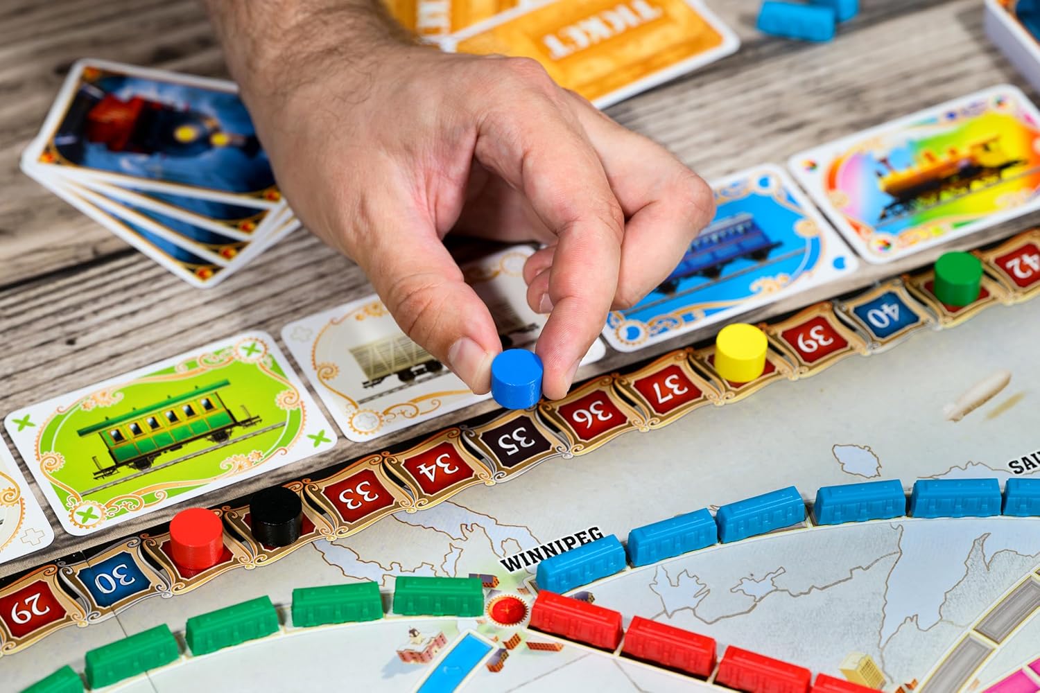 Hand places a blue scoring marker onto the numbered track of a train-themed board game