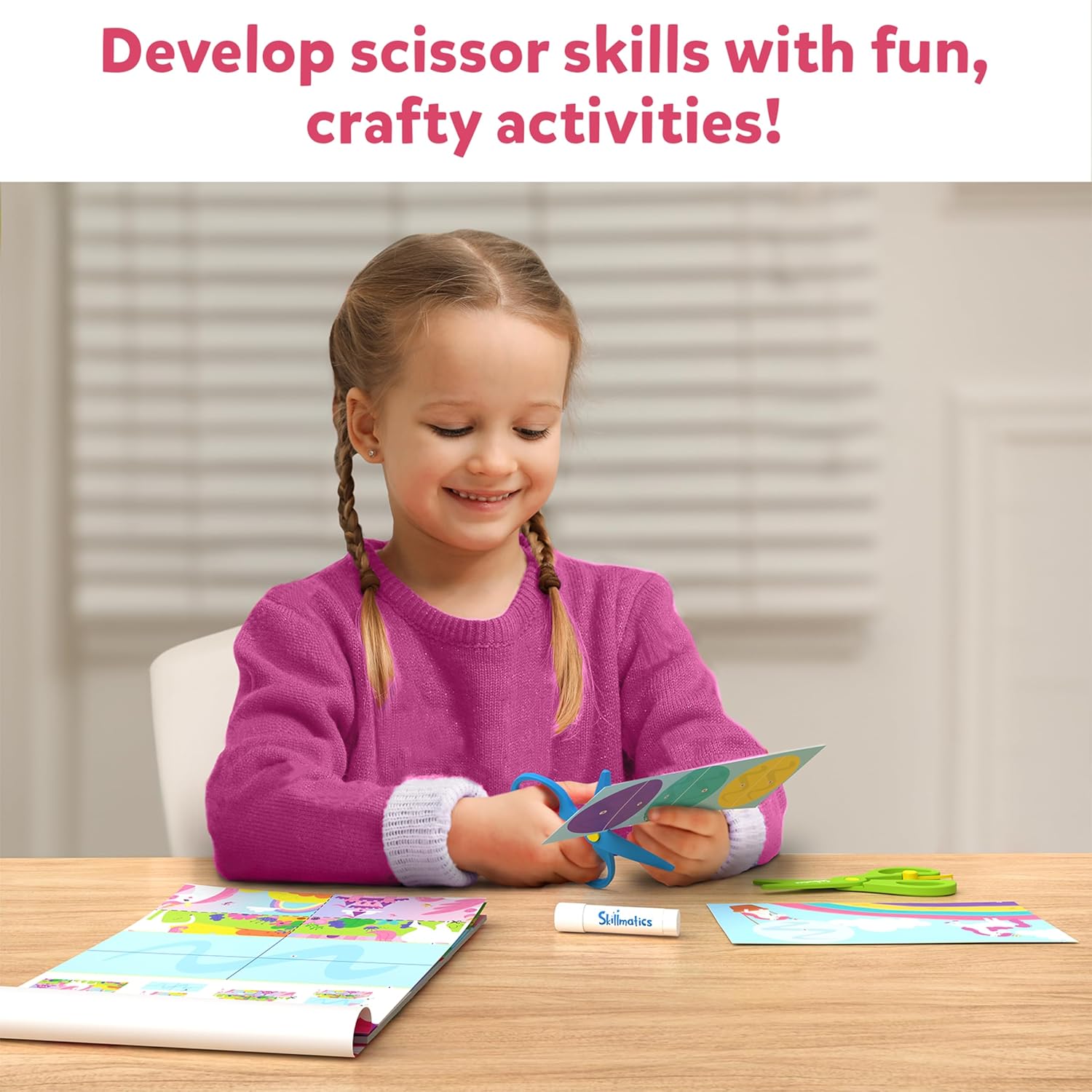 Happy girl practicing scissor skills, cutting colorful paper with blue safety scissors