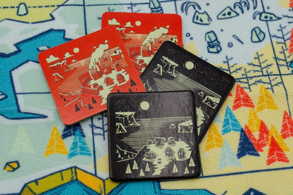 Four overlapping square game tiles show red day and black night village scenes on a colourful mat.