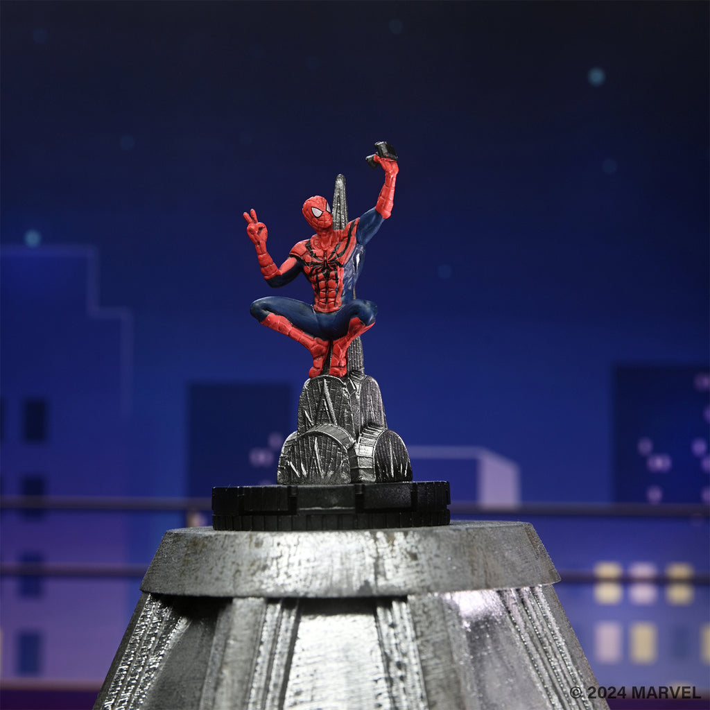 Spider-Man figurine taking a selfie with a peace sign atop a building, night city backdrop