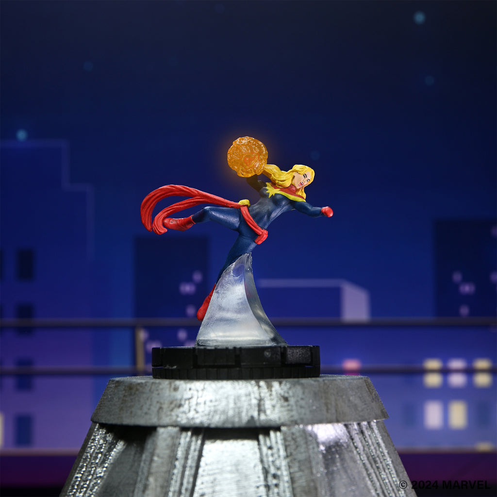 A Captain Marvel figure in a dynamic pose, flying with a glowing energy orb against a night city skyline