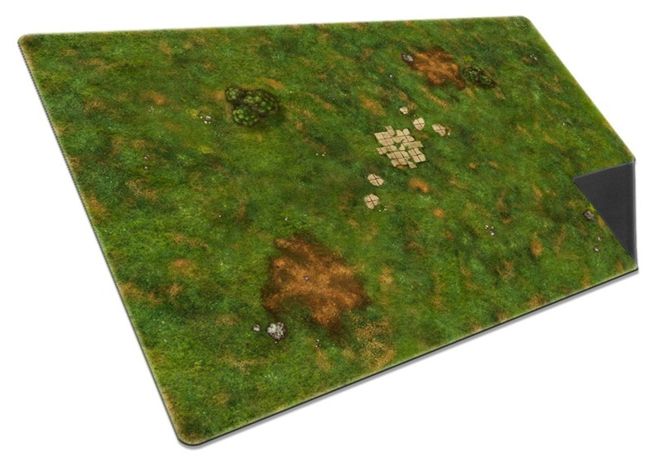 Overhead view of the Onus Traianus Meadow playmat, illustrating dense green grass texture, brown dirt areas, and a formation of ruined stone pavers