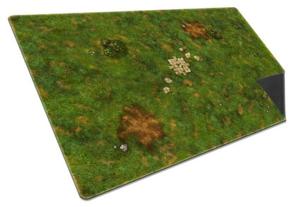 Overhead view of the Onus Traianus Meadow playmat, illustrating dense green grass texture, brown dirt areas, and a formation of ruined stone pavers