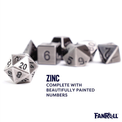A single brushed antique silver D20 dice with black numbers is sharp in the foreground, with the rest of the polyhedral metal dice set scattered and blurred behind it