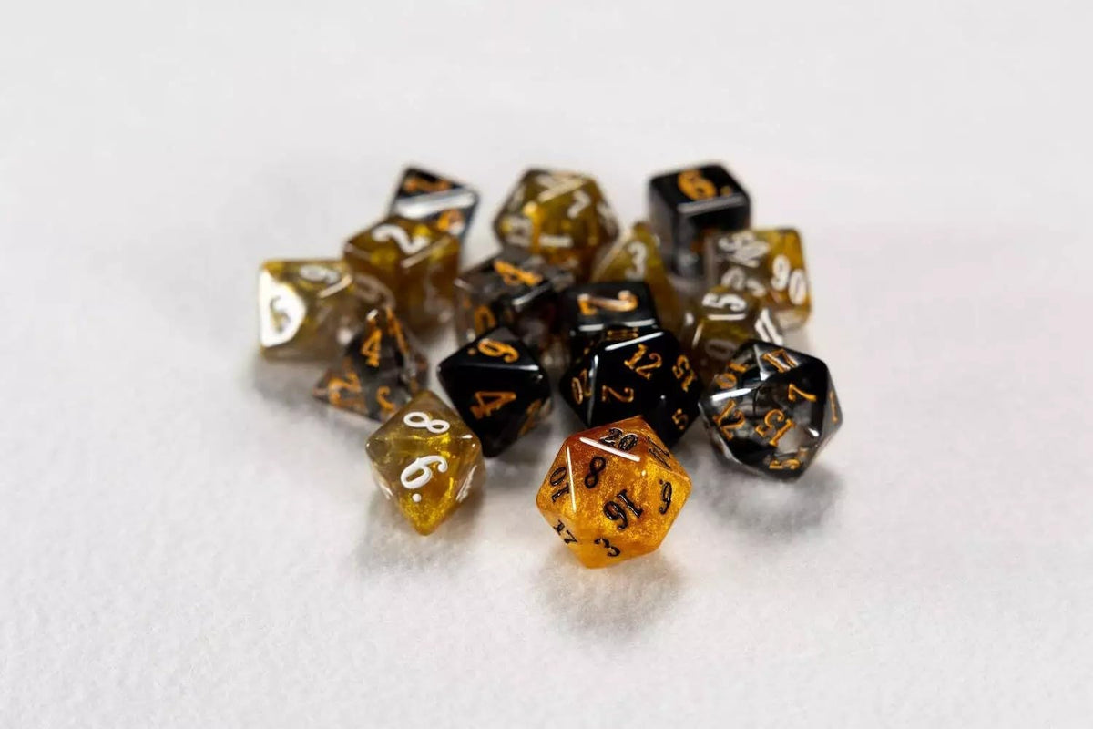 A scattering of polyhedral dice in black and translucent gold colors, part of The Game Master Epic Dice Set, on a white surface