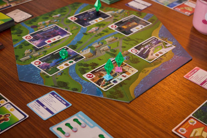 A detailed close-up of The Sims board game setup shows the colorful map, various location cards, and three translucent green plumbob player pieces resting on a brown wooden table