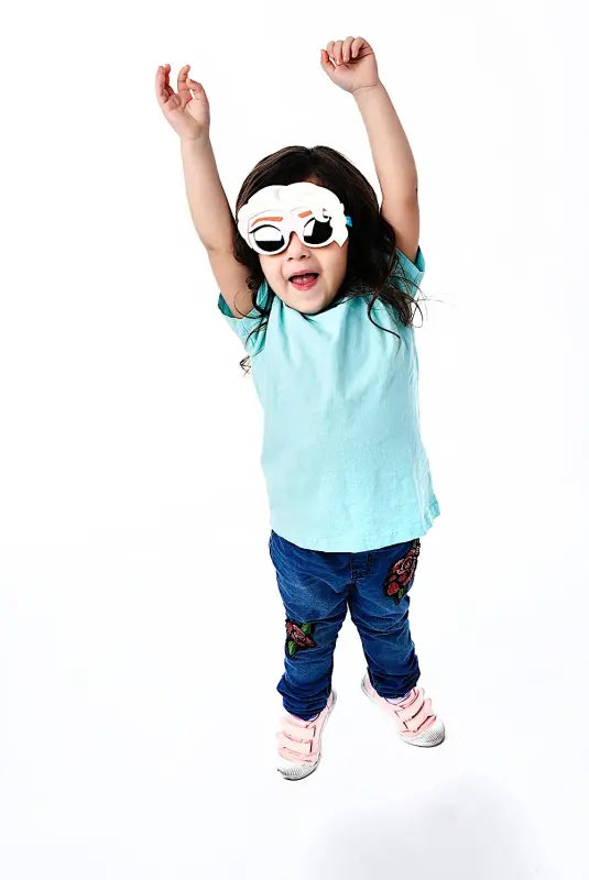 Young girl in Frozen Elsa sunglass mask light blue t-shirt and embroidered jeans jumping with arms raised