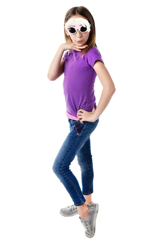 Girl in purple shirt and blue jeans poses with sunglasses featuring white sculpted hair details